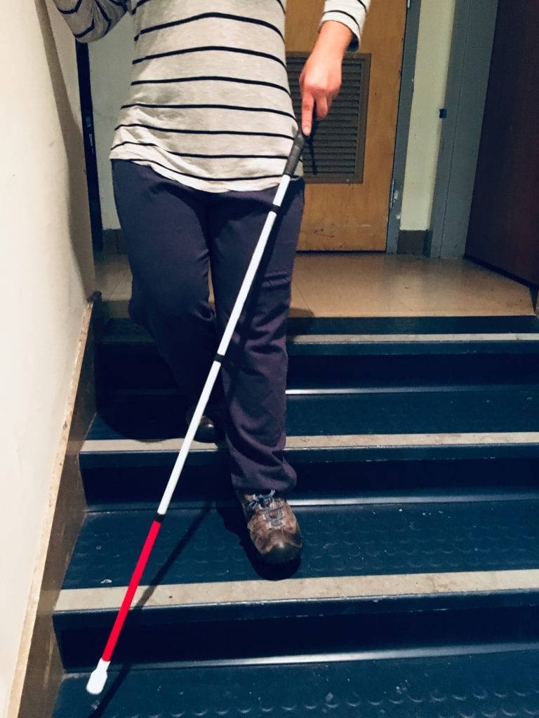 Girl going down stairs using a white mobility cane