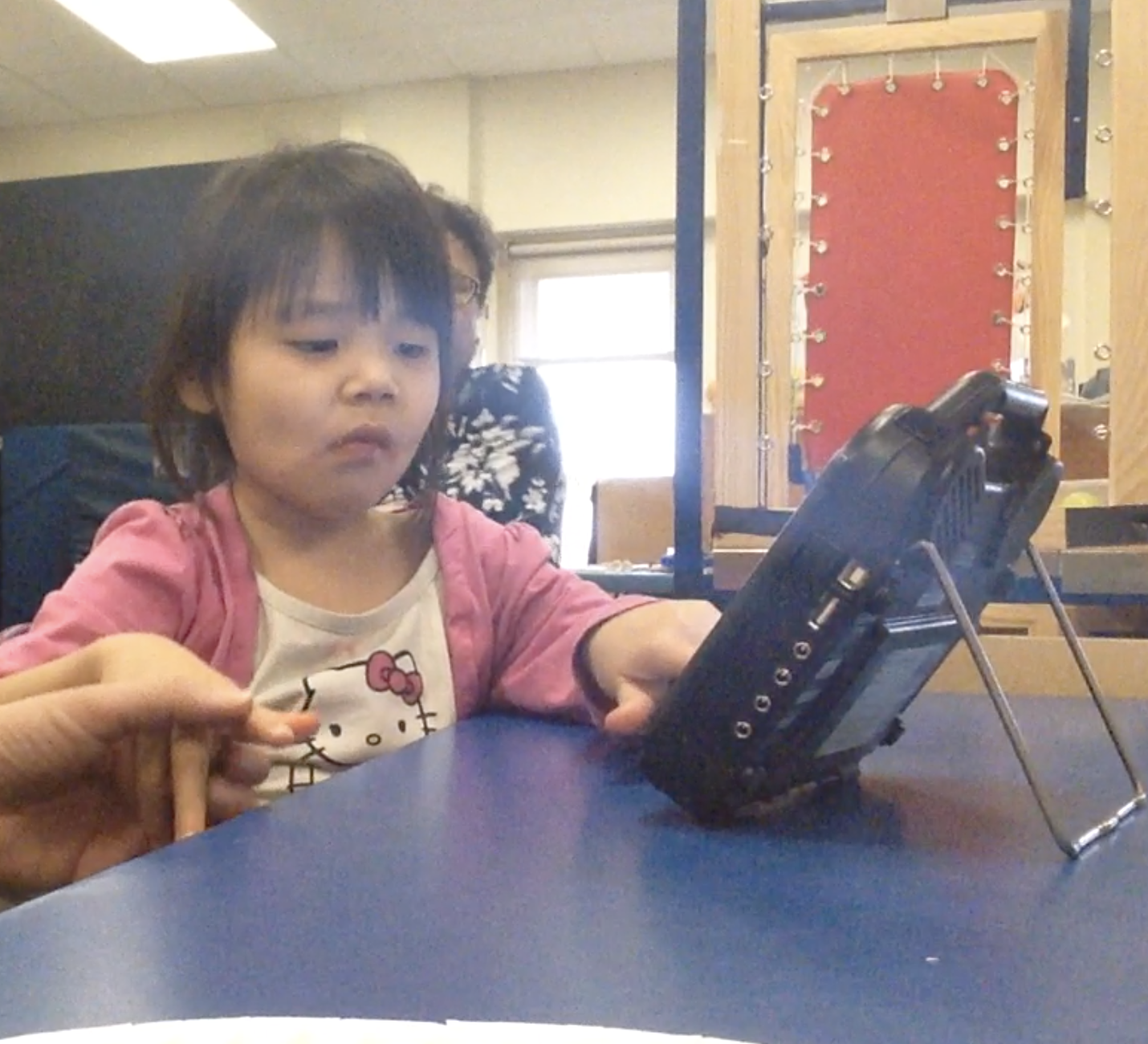 A young girl is learning how to communicate with an AAC device with the help of her teacher.
