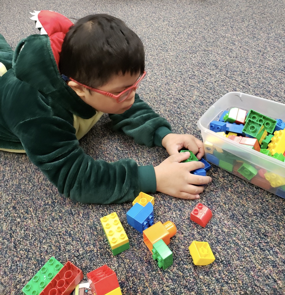Young student with Down Syndrome playing with legos on the floor.